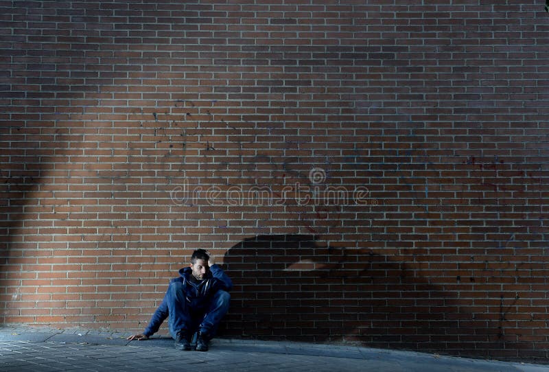 Giovane uomo senza lavoro disperato che il lavoro perso ha perso nella depressione che si siede sull'angolo di strada al suolo immagini stock libere da diritti Giovane uomo senza lavoro disperato che il lavoro perso ha perso nella depressione che si siede sull'angolo di strada al suolo immagini stock libere da diritti