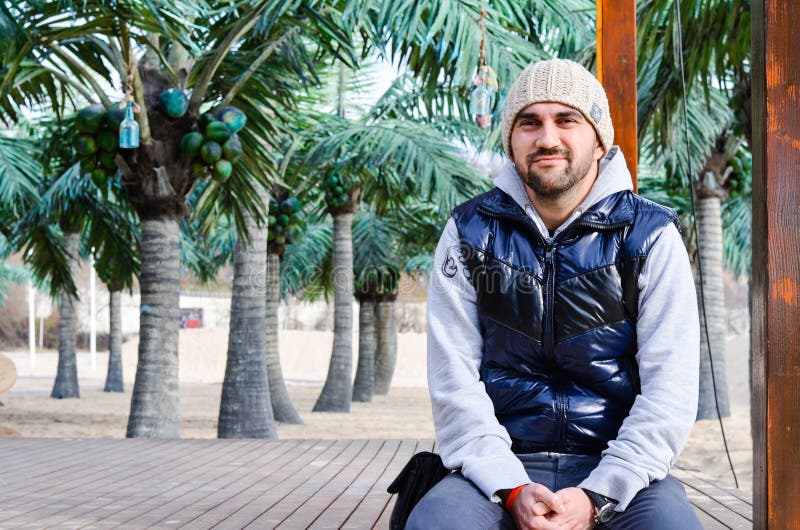 giovane uomo sorridente barbuto che si siede sulla spiaggia tropicale con le palme fotografia stock giovane uomo sorridente barbuto che si siede sulla spiaggia tropicale con le palme fotografia stock