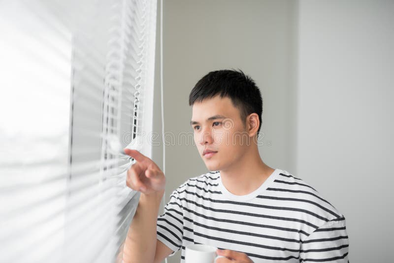 Giovane uomo spensierato bello vicino alla finestra integrale moderna che gode di una tazza di caff? mentre guardando fuori, buon immagini stock Giovane uomo spensierato bello vicino alla finestra integrale moderna che gode di una tazza di caff? mentre guardando fuori, buon immagini stock