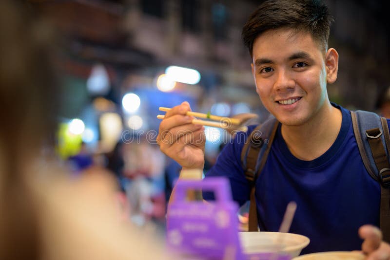 Giovane uomo turistico asiatico che esplora a Chinatown mentre mangiando minestra di pasta immagini stock libere da diritti Giovane uomo turistico asiatico che esplora a Chinatown mentre mangiando minestra di pasta immagini stock libere da diritti