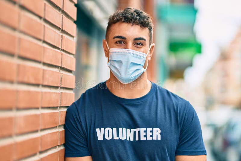 Giovane volontario ispanico con una maschera medica in piedi per la città fotografia stock libera da diritti