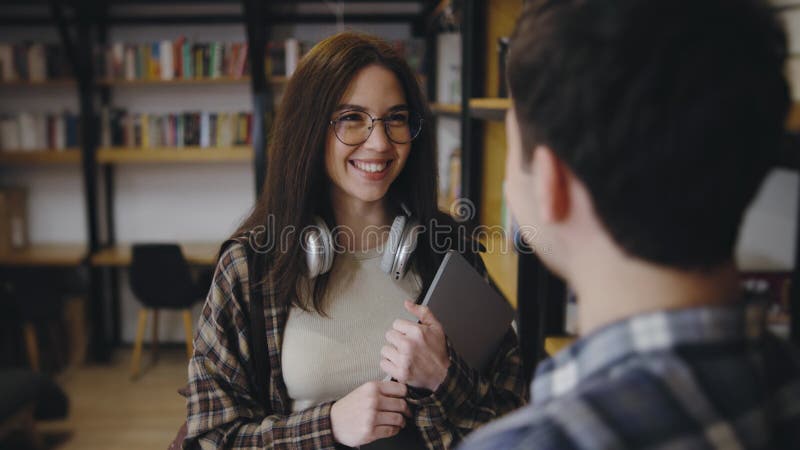 Giovani adulti impegnati in una conversazione amichevole in una biblioteca accogliente che mette in evidenza un'atmosfera di studi video d archivio