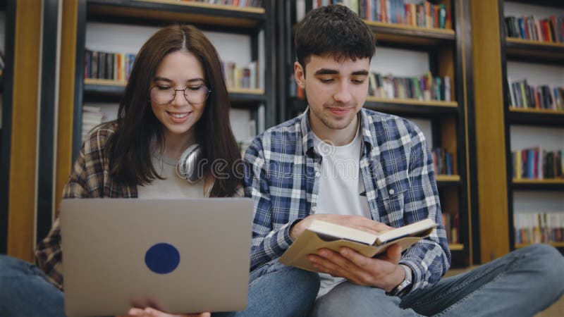 Giovani adulti impegnati in una sessione di studio in una biblioteca con scaffali e un'atmosfera accogliente che mostra il lavoro video d archivio