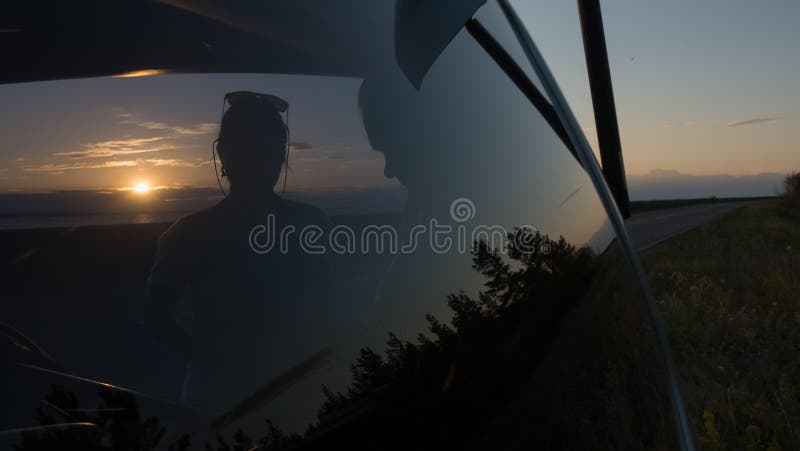 Giovani coppie al tronco di un'automobile al tramonto vicino alla strada immagine stock Giovani coppie al tronco di un'automobile al tramonto vicino alla strada immagine stock