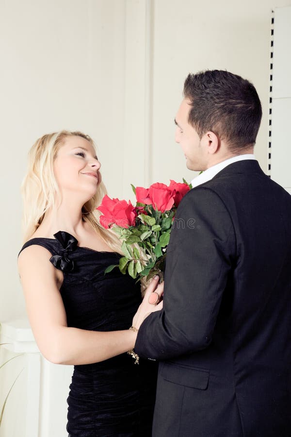 Loving young couple smiling at each other over a large bouquet of red roses as they stand looking into each others eyes. Loving young couple smiling at each other over a large bouquet of red roses as they stand looking into each others eyes