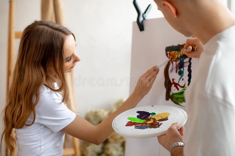 Giovani coppie carine dipingono entusiasticamente su tela utilizzando pennelli a colori in prossimità di una scala. terapia artist fotografia stock