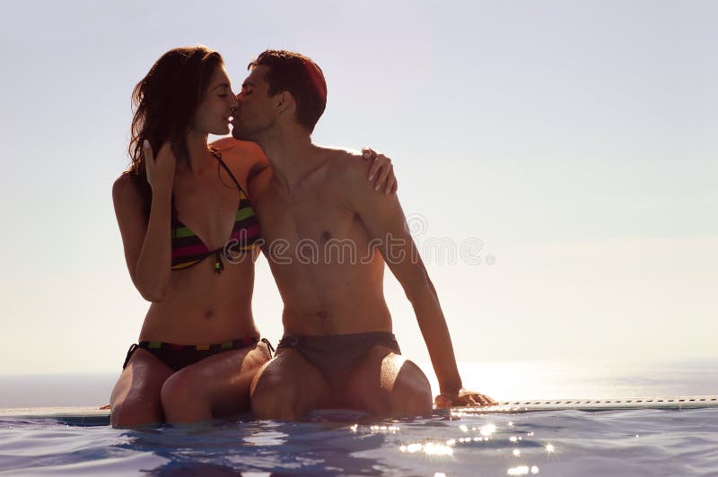 Giovani coppie che baciano in una piscina di infinito Coppie di luna di miele alla località di soggiorno di lusso vacanza romanti immagini stock Giovani coppie che baciano in una piscina di infinito Coppie di luna di miele alla località di soggiorno di lusso vacanza romanti immagini stock