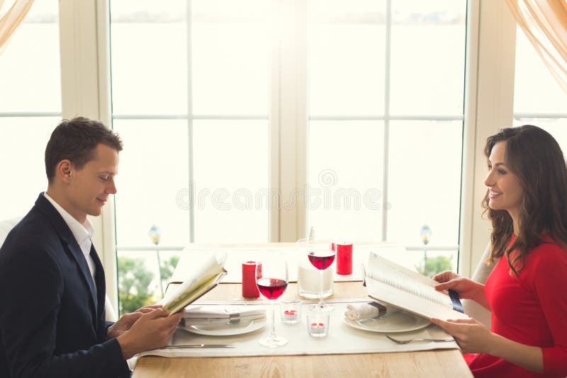 Giovani coppie che hanno cena romantica nel menu di osservazione del ristorante fotografia stock libera da diritti Giovani coppie che hanno cena romantica nel menu di osservazione del ristorante fotografia stock libera da diritti