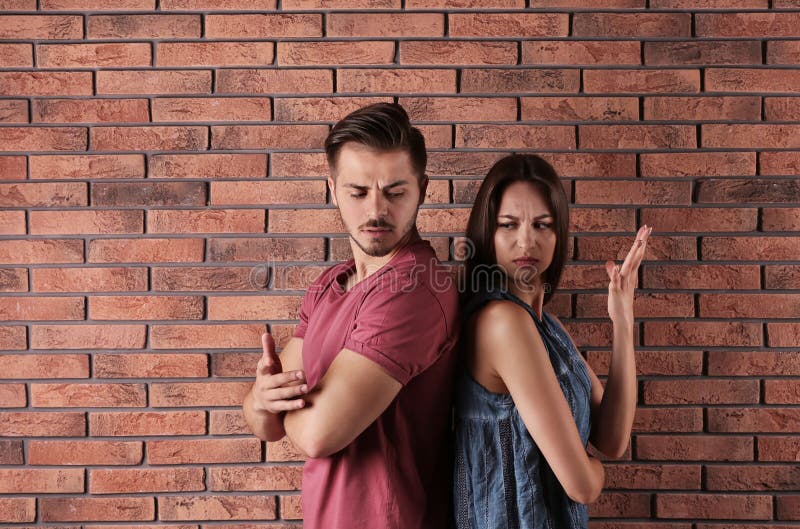 Giovani coppie che hanno discussione vicino al muro di mattoni immagine stock Giovani coppie che hanno discussione vicino al muro di mattoni immagine stock