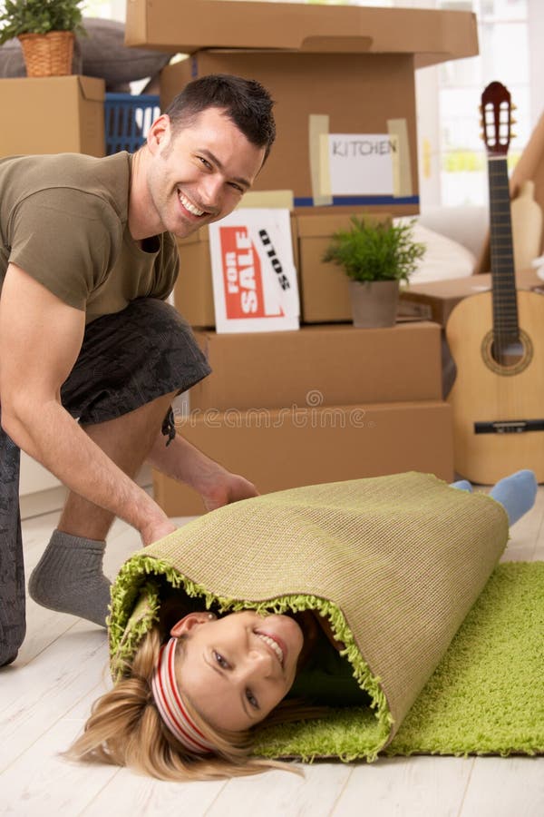 Young couple having fun at moving house, laughing man rolling girlfriend into carpet. Young couple having fun at moving house, laughing man rolling girlfriend into carpet.