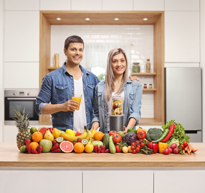 Giovani coppie che posano dietro un contatore di cucina con la frutta e le verdure