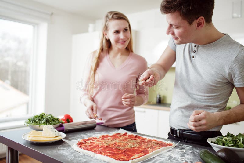 Giovani coppie che preparano la pizza nella cucina immagine stock libera da diritti Giovani coppie che preparano la pizza nella cucina immagine stock libera da diritti