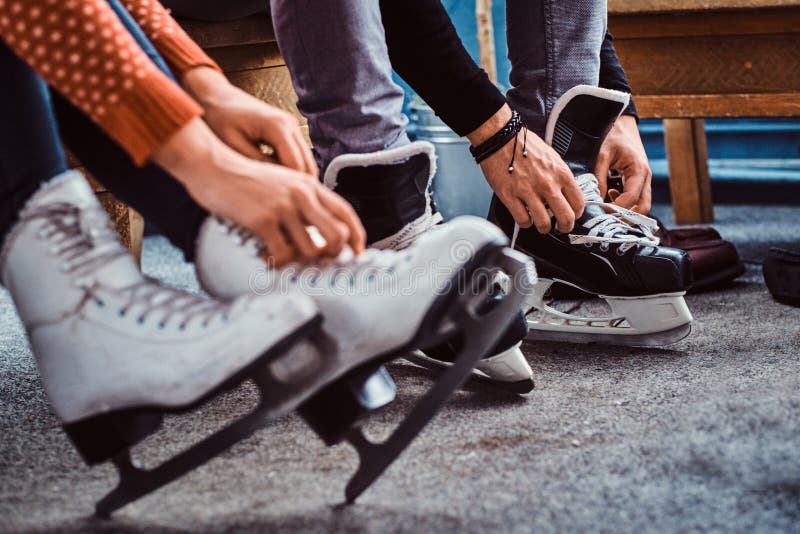 Giovani coppie che preparano a pattinare Foto del primo piano delle loro mani che legano i laccetti dei pattini del hockey su ghi