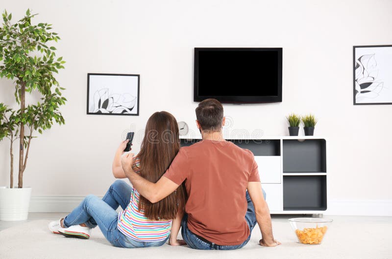 Giovani coppie che si siedono sul pavimento e sulla TV di sorveglianza immagini stock Giovani coppie che si siedono sul pavimento e sulla TV di sorveglianza immagini stock