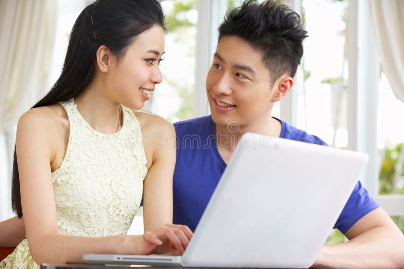 Giovani coppie cinesi allo scrittorio ed al computer portatile usando immagini stock libere da diritti Giovani coppie cinesi allo scrittorio ed al computer portatile usando immagini stock libere da diritti