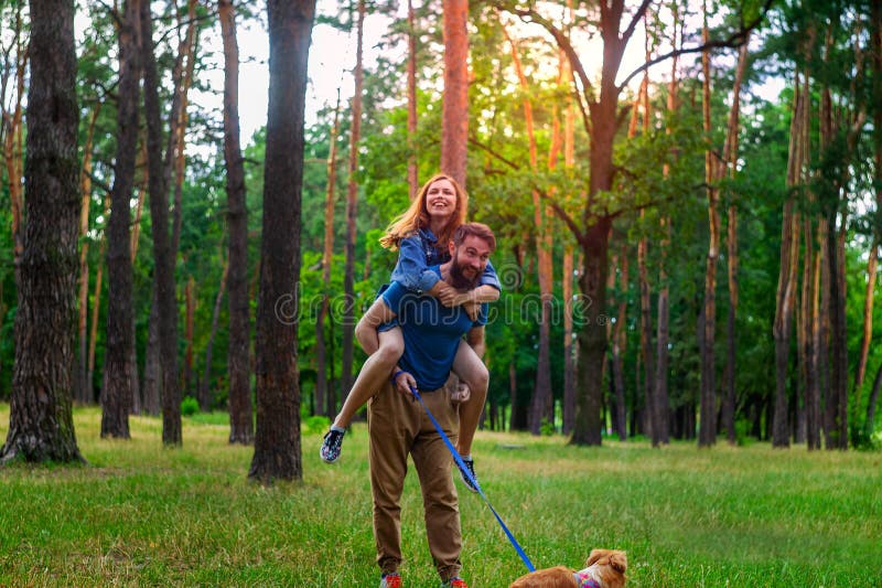 Giovani coppie con un cane che cammina lungo il parco di autunno fotografia stock libera da diritti Giovani coppie con un cane che cammina lungo il parco di autunno fotografia stock libera da diritti