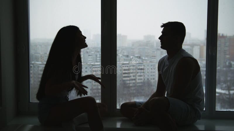 Giovani coppie della famiglia che si siedono sul davanzale, emozionalmente sulla conversazione, sulla discussione e sul gesticola immagine stock libera da diritti Giovani coppie della famiglia che si siedono sul davanzale, emozionalmente sulla conversazione, sulla discussione e sul gesticola immagine stock libera da diritti