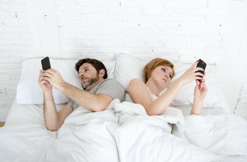 Giovani coppie facendo uso del telefono cellulare a letto che si trascura nei problemi di comunicazione di relazione immagine stock Giovani coppie facendo uso del telefono cellulare a letto che si trascura nei problemi di comunicazione di relazione immagine stock