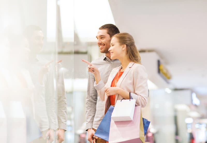 Giovani coppie felici con i sacchetti della spesa in centro commerciale immagini stock Giovani coppie felici con i sacchetti della spesa in centro commerciale immagini stock