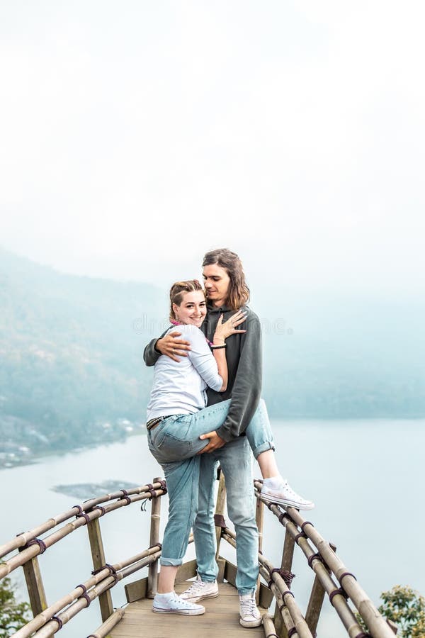 Giovani coppie felici dei turisti sul ponte di legno con fondo tropicale Lago Isola di Bali fotografia stock Giovani coppie felici dei turisti sul ponte di legno con fondo tropicale Lago Isola di Bali fotografia stock
