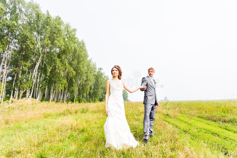 Giovani coppie nella sposa e nello sposo di amore che posano in un campo con erba gialla nel loro giorno delle nozze di estate fotografie stock libere da diritti Giovani coppie nella sposa e nello sposo di amore che posano in un campo con erba gialla nel loro giorno delle nozze di estate fotografie stock libere da diritti