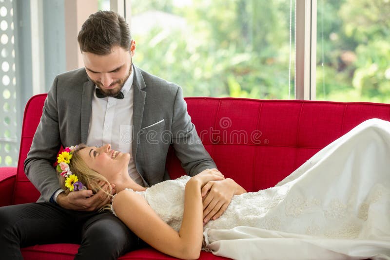 giovani coppie nella sposa e nello sposo di nozze di amore che si riposano sul sofà rosso che se esamina insieme newlyweds Ritrat fotografia stock giovani coppie nella sposa e nello sposo di nozze di amore che si riposano sul sofà rosso che se esamina insieme newlyweds Ritrat fotografia stock