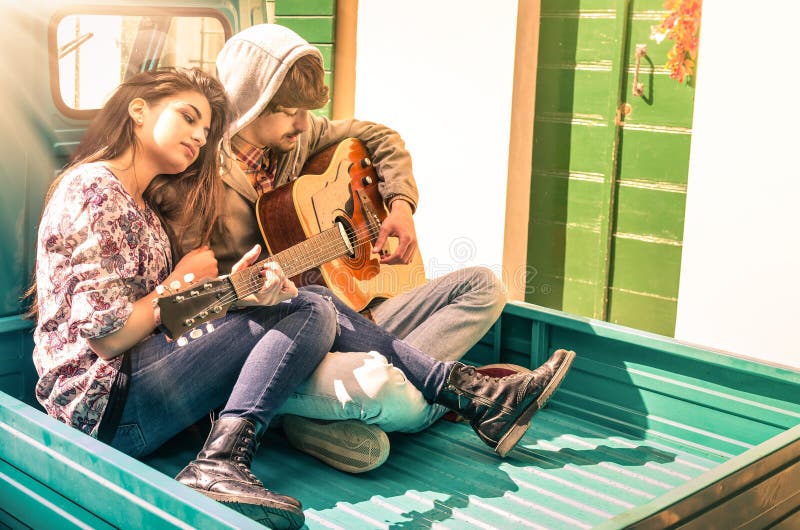 Giovani coppie romantiche degli amanti che giocano chitarra all'aperto immagine stock libera da diritti Giovani coppie romantiche degli amanti che giocano chitarra all'aperto immagine stock libera da diritti