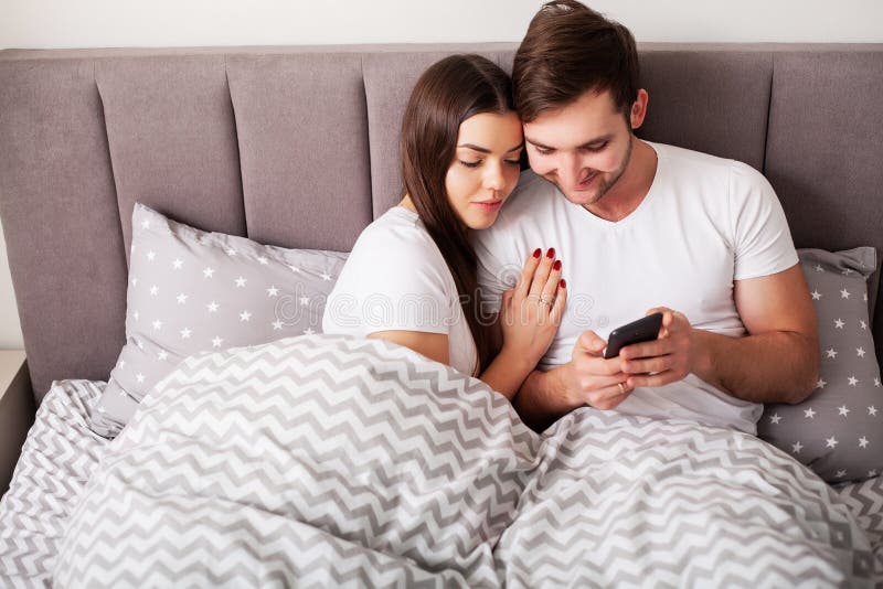 Giovani coppie sorridenti che prendono insieme selfie nella camera da letto fotografie stock Giovani coppie sorridenti che prendono insieme selfie nella camera da letto fotografie stock