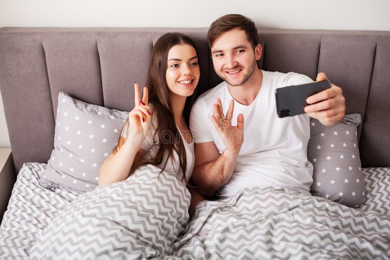Giovani coppie sorridenti che prendono insieme selfie nella camera da letto immagini stock libere da diritti Giovani coppie sorridenti che prendono insieme selfie nella camera da letto immagini stock libere da diritti
