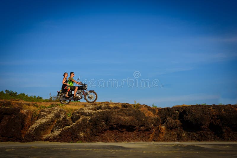 Giovani coppie su un motociclo su terra rocciosa Tipo felice e ragazza che viaggiano su una motocicletta fotografia stock Giovani coppie su un motociclo su terra rocciosa Tipo felice e ragazza che viaggiano su una motocicletta fotografia stock