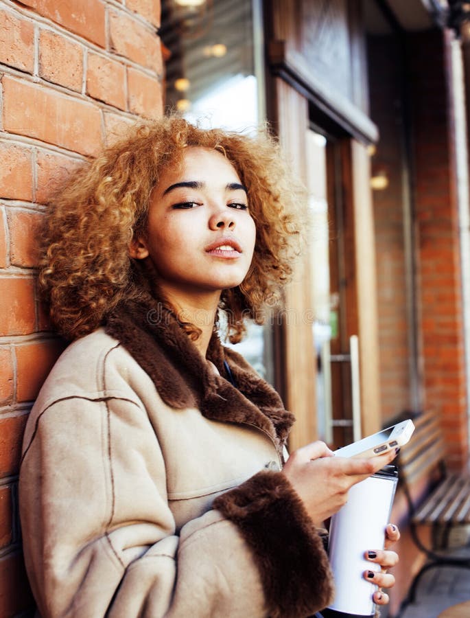 Young pretty african american woman drinking coffee outside in cafe, modern business woman lifestyle concept close up. Young pretty african american woman drinking coffee outside in cafe, modern business woman lifestyle concept close up