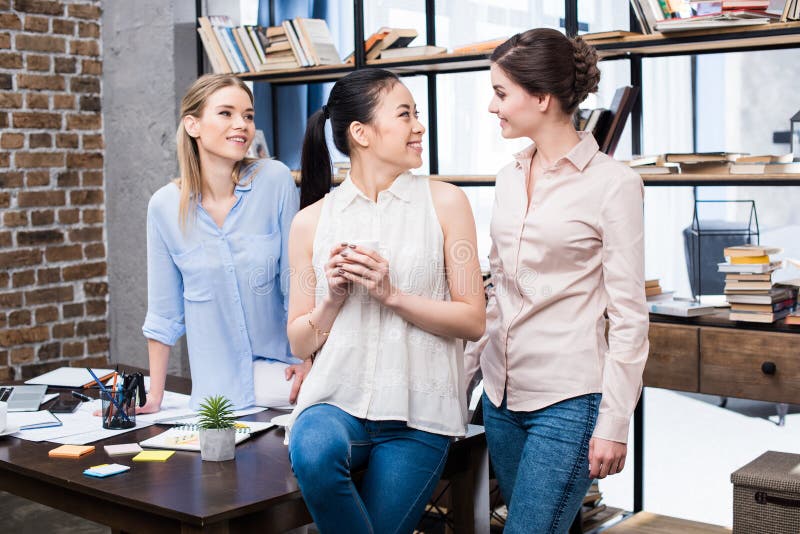 Giovani donne di affari che parlano nel luogo di lavoro mentre avendo pausa caffè fotografia stock Giovani donne di affari che parlano nel luogo di lavoro mentre avendo pausa caffè fotografia stock
