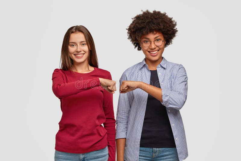 Giovani donne multietniche si battono a pugni l'un l'altro, si mostrano amichevoli, hanno espressioni positive immagini stock libere da diritti