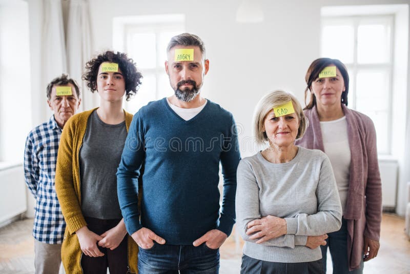 A portrait of young and old people standing with negative emotions adhesive notes during group therapy. A portrait of young and old people standing with negative emotions adhesive notes during group therapy.
