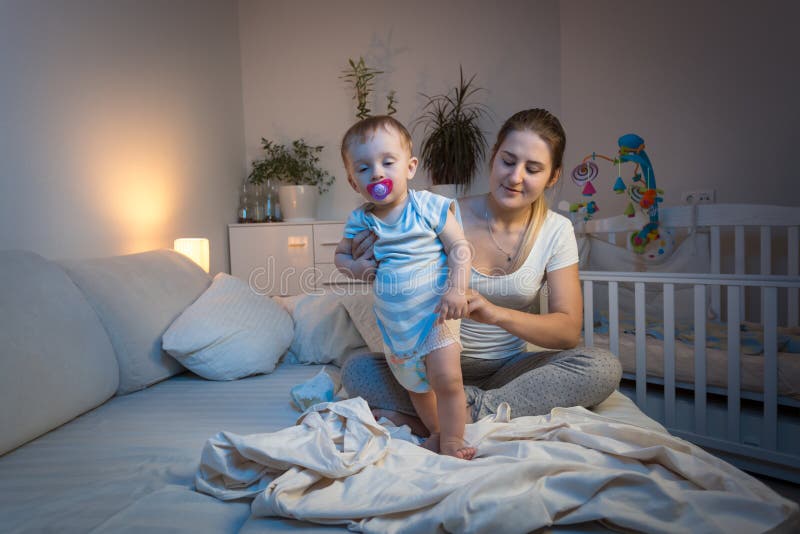Giovani pannolini cambianti preoccupantesi della madre al suo neonato sonnolento prima di andare a dormire immagine stock Giovani pannolini cambianti preoccupantesi della madre al suo neonato sonnolento prima di andare a dormire immagine stock