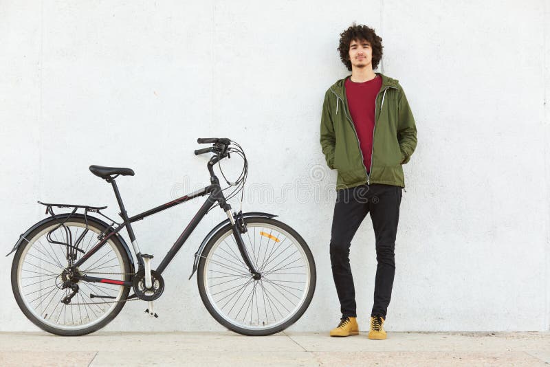 Giovani pantaloni a vita bassa attivi piacevoli che sono nel giro di guida, avendo fermata da rilassarsi, stando vicino alla sua immagini stock Giovani pantaloni a vita bassa attivi piacevoli che sono nel giro di guida, avendo fermata da rilassarsi, stando vicino alla sua immagini stock