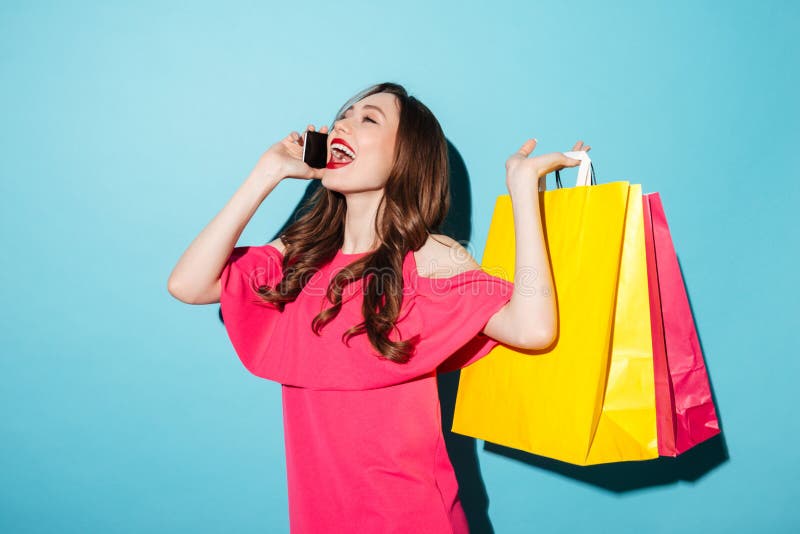 Giovani sacchetti della spesa castana felici della tenuta della donna che parlano dal telefono fotografie stock Giovani sacchetti della spesa castana felici della tenuta della donna che parlano dal telefono fotografie stock
