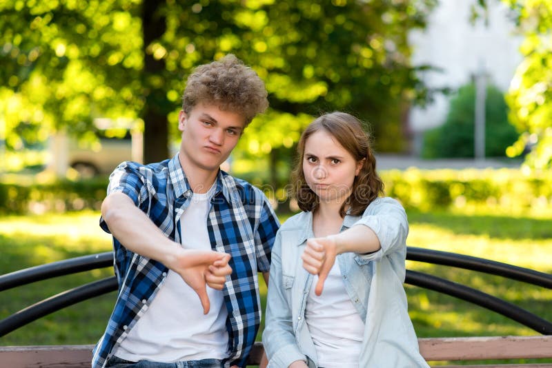 Giovani studenti del tipo con una ragazza di estate in parco in natura Gestures il suo dito giù disco Il concetto di fotografia stock libera da diritti Giovani studenti del tipo con una ragazza di estate in parco in natura Gestures il suo dito giù disco Il concetto di fotografia stock libera da diritti