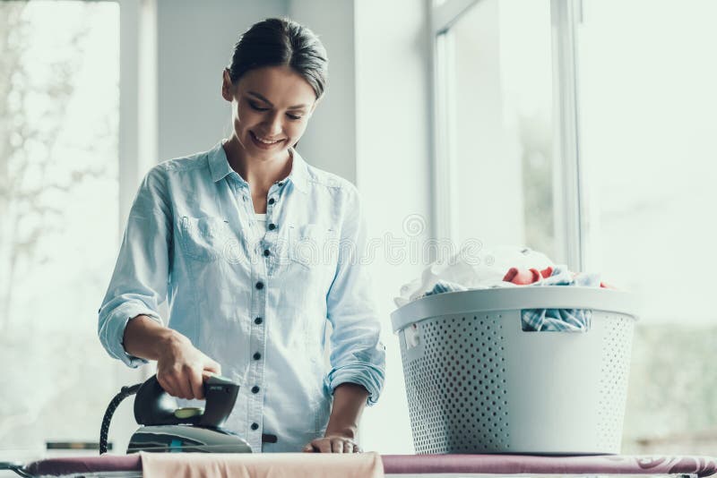 Giovani vestiti rivestenti di ferro sorridenti della donna dopo la lavanderia fotografia stock Giovani vestiti rivestenti di ferro sorridenti della donna dopo la lavanderia fotografia stock