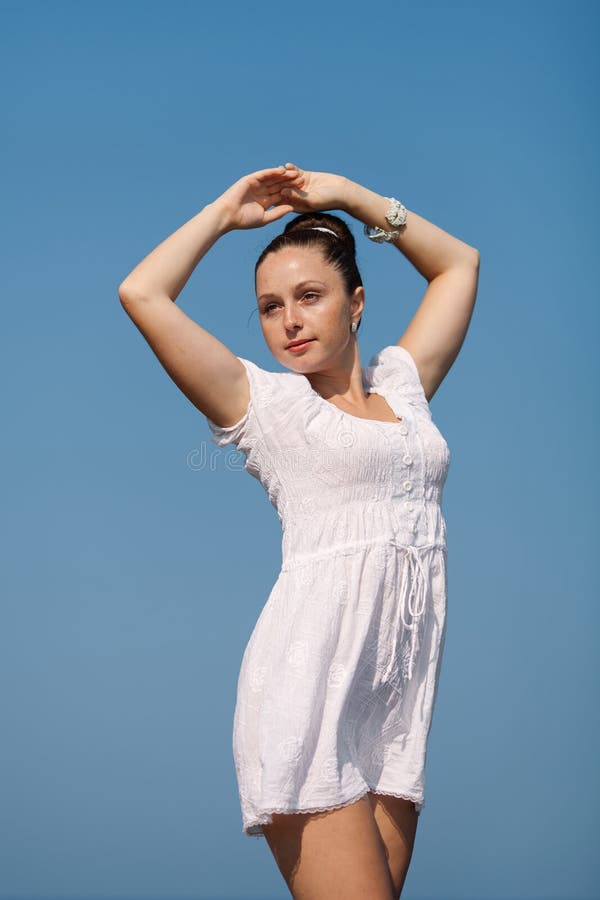 Girl against of sky. Young woman in white posing with hands raised outdoors