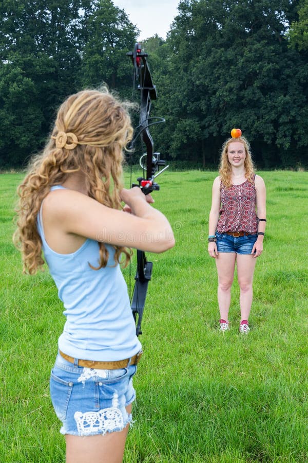 Girl aiming arrow of compound bow at apple on head of woman stock image Girl aiming arrow of compound bow at apple on head of woman stock image