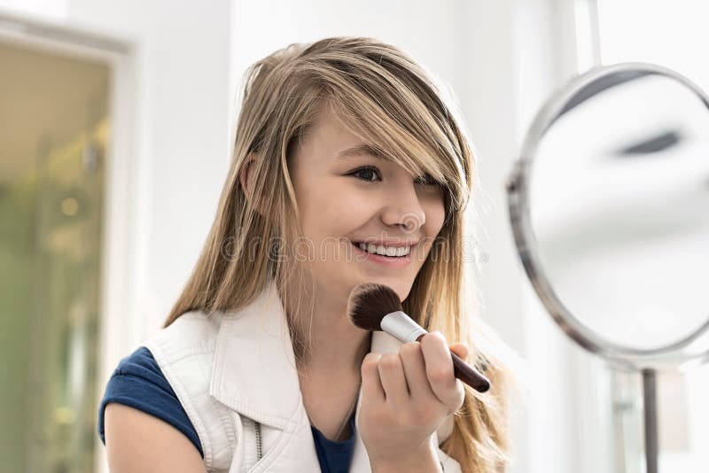 Girl applying makeup in front of mirror at home