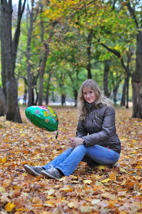 Girl in autumn park with balloon sits on the stump