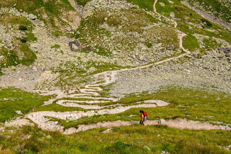 Girl backpacker on zigzagged hiking path serpentines, Austria mountains, Alps