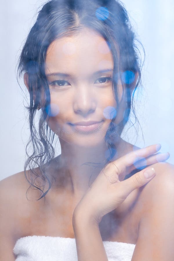 Nice Asian woman in the bathroom behind the frosted glass with wet curly hair. Nice Asian woman in the bathroom behind the frosted glass with wet curly hair