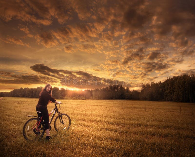 Girl on the bicycle. In field on sunset Girl on the bicycle. In field on sunset