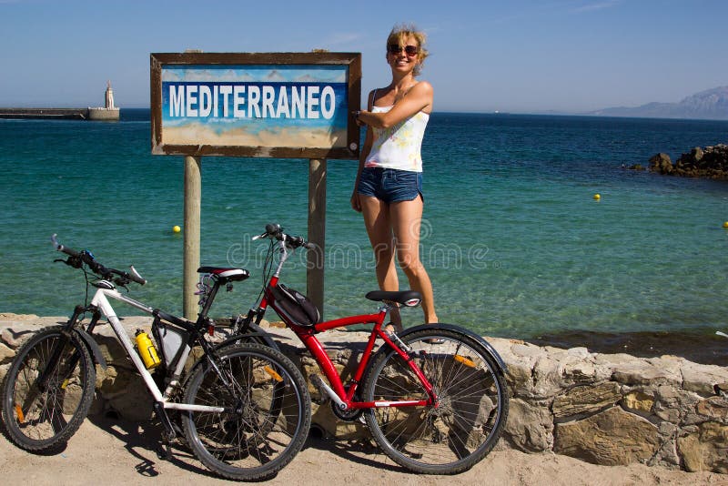 Girl with 2 bicycles against Mediterraneo sign at seaside Spain