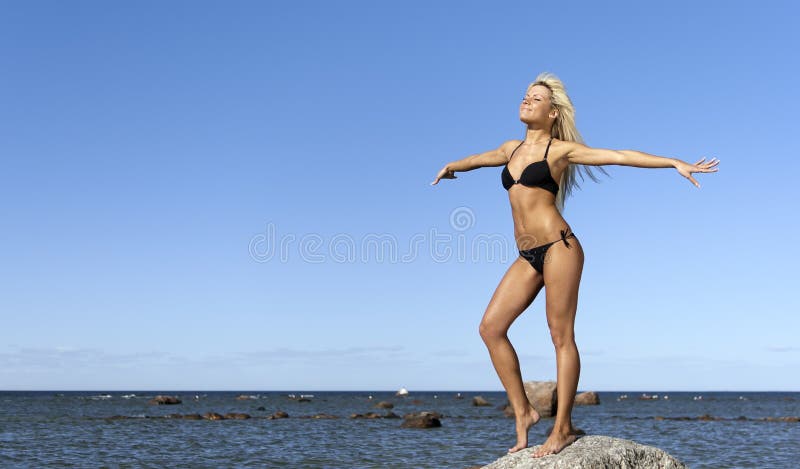 Girl in bikini posing on a rock near the sea