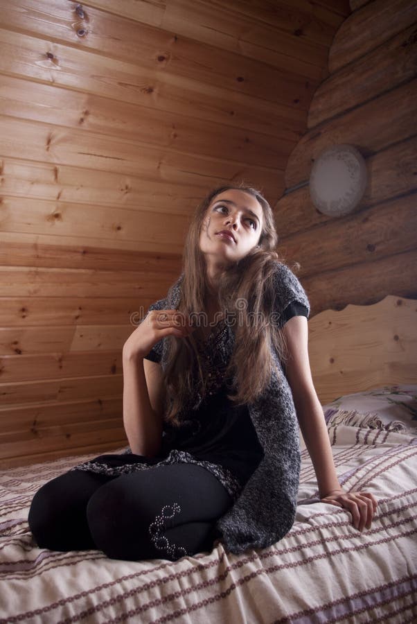 Girl in black jersey sitting on vintage bed in wooden house.