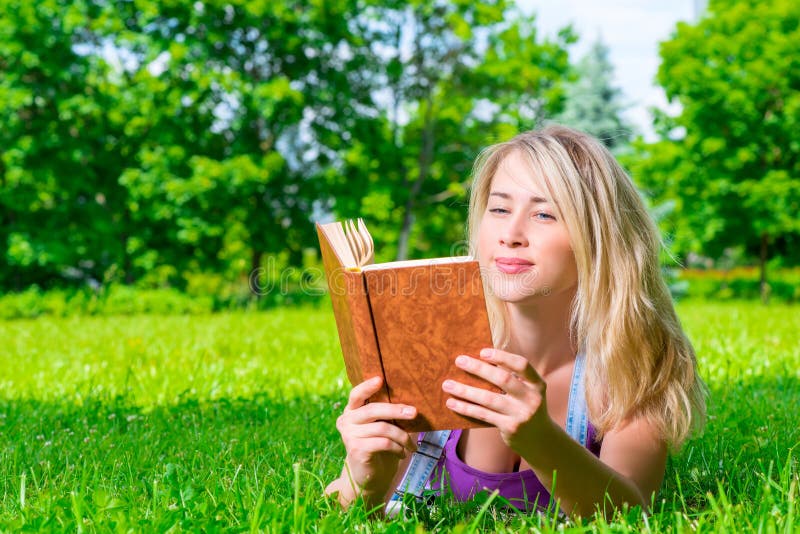 Girl with a book lying on a green meadow